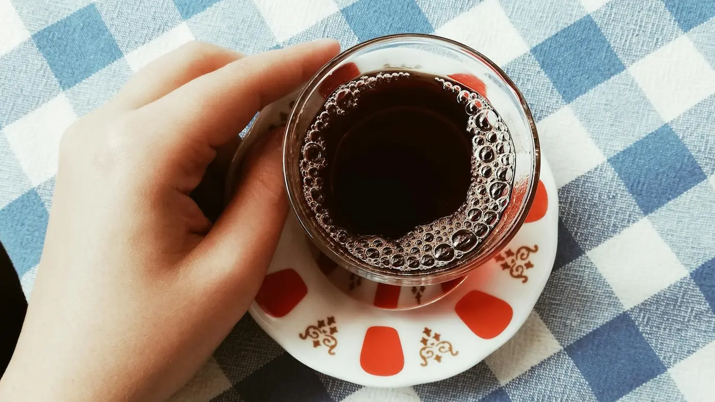 Tasse de café à la chicorée tenue à la main sur une nappe à carreaux bleus